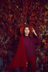 Woman in a red hat and red sweater stands on a background of orange leaves grapes wall autumn