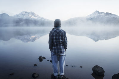 Rear view of woman standing on rock against lake and mountain in foggy weather