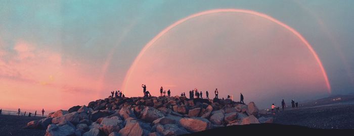 People on rock against sky during sunset