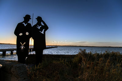 Silhouette men standing at beach against clear sky