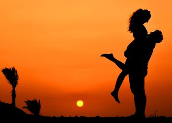 Silhouette couple standing on field against sky during sunset