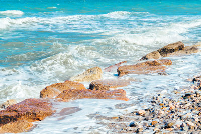 Surface of sea waves during windy summer day, sea shore with pebble stones and cutwater.