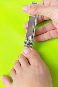 Close-up of person cutting fingernails over green background