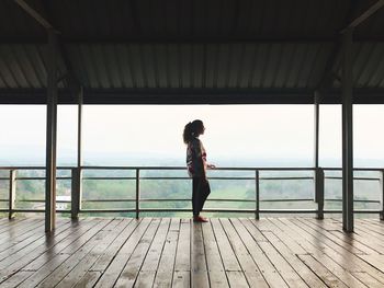 Side view of woman standing on wooden railing