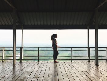 Side view of woman standing on wooden floor by railing