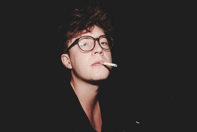 Portrait of young man with cigarette standing outdoors at night
