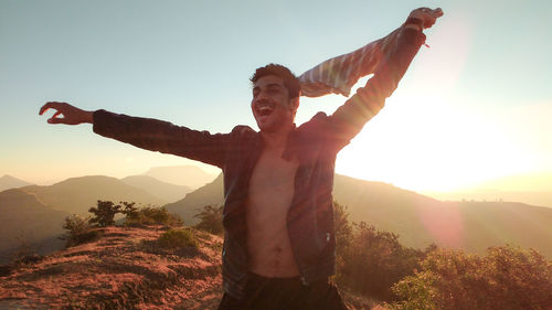 Man with arms outstretched standing on mountain against sky