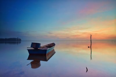 Boat moored on sea against sky during sunset