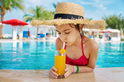 Girl drinking orange juice at pool side