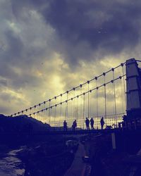 People walking on bridge against sky during sunset