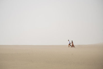 Man on sand dune in desert against sky