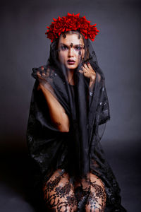 Portrait of young woman covered with fabric against black background