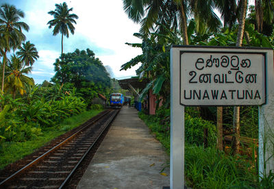 Information sign by railroad tracks against sky