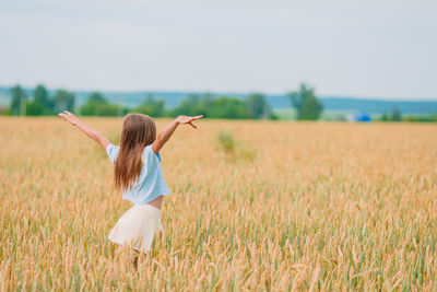 Rear view of girl with arms outstretched standing on field