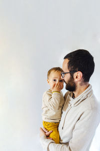 Daddy with his surprised son covering his mouth in arms on white background. father and baby 