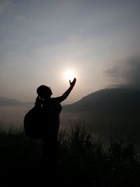 Optical illusion of silhouette woman holding sun on mountain against sky during sunset