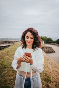 Full length of young woman using mobile phone against sky