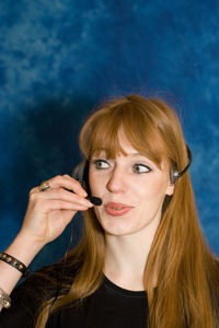 Confident businesswoman talking on headset against blue wall