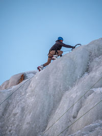 Low angle view of man climbing on mountain against sky