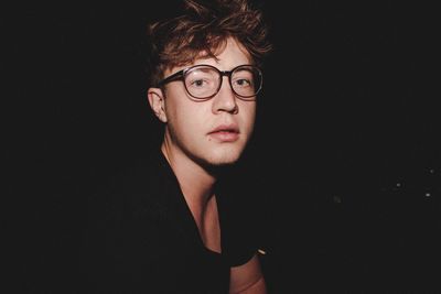 Portrait of young man wearing eyeglasses against black background