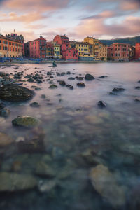 Buildings by sea against sky during sunset