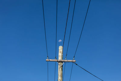 Low angle view of electricity pylon against clear blue sky