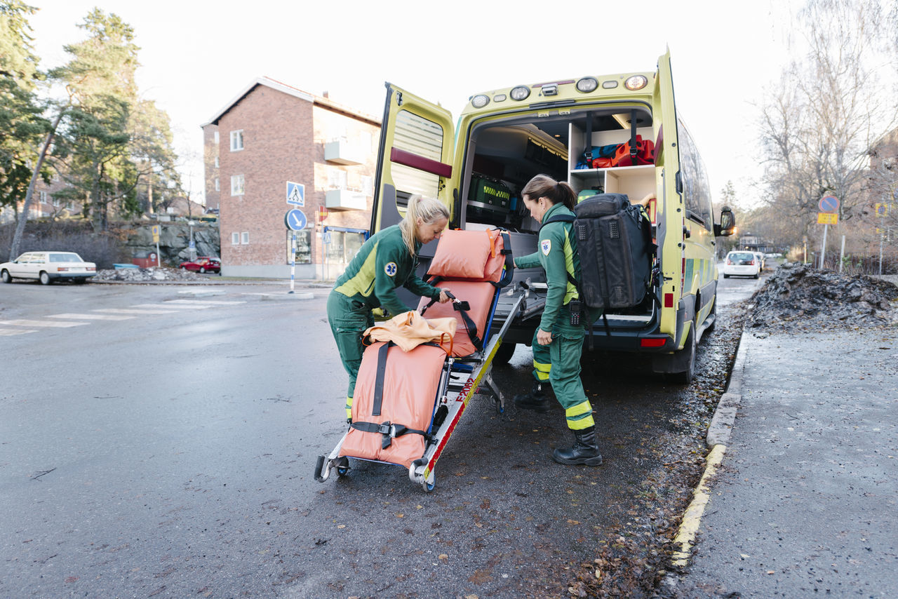 Side view of female paramedics preparing stretcher outside ambulance on road