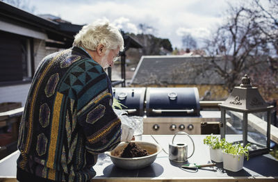 Senior man pouring fertilizer in container at table on sunny day