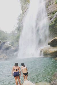 Rear view of woman standing by waterfall against sky