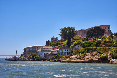 Buildings by sea against clear blue sky