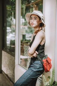 Portrait of beautiful young woman standing against window