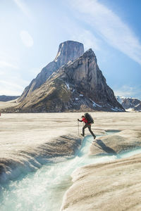 Backpacker hikes over glacial river below mount asgard, baffin island.