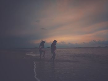 Women on beach against sky during sunset