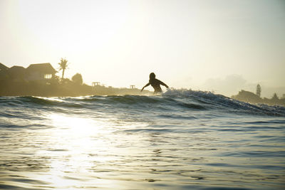 Silhouette man surfing in sea against sky during sunset