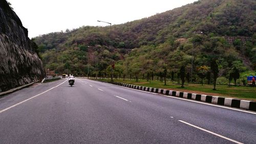 Road by trees on mountain against sky