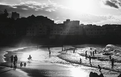 Silhouette people enjoying at beach against buildings