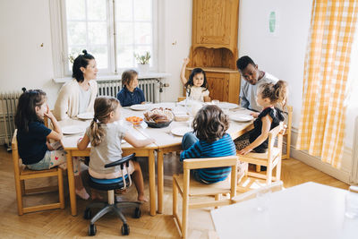 Teachers and students sitting at table during lunch break in classroom