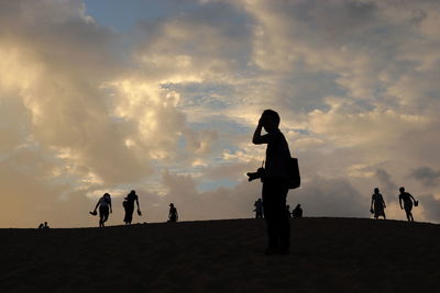 Silhouette people on land against sky during sunset