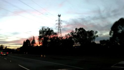 Silhouette trees by road against sky during sunset