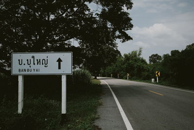 Road sign by trees against sky