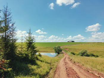 Empty road amidst field against sky