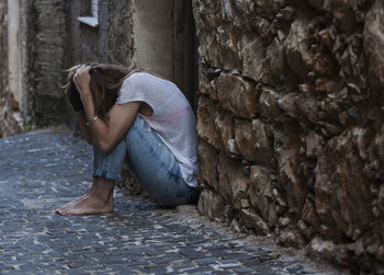 Full length of woman sitting on street by wall