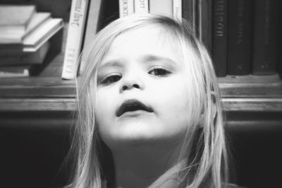 Close-up portrait of cute girl standing against bookshelf