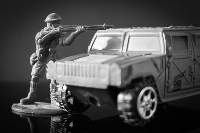 Figurine shooting with rifle by car over black background