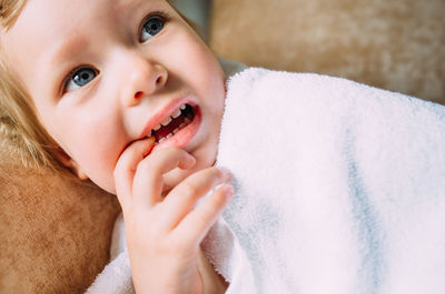 Cute baby in a big white towel. holds fingers in the mouth.