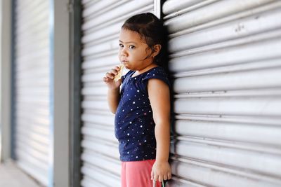 Girl eating food while standing by shutter