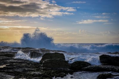 Waves splashing on rocks against sky