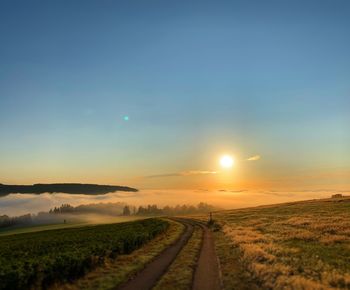 Road amidst field against sky during sunset