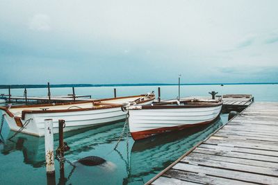 Boats moored by pier against sky