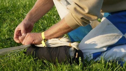 Midsection of man tying rope while kneeling on field